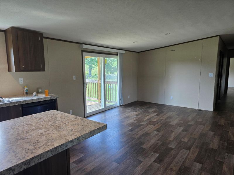 Open-concept living area featuring wood-finish flooring, light-toned walls, and a sliding glass door leading to an outdoor deck Open-concept living area featuring wood-finish flooring, light-toned walls, and a sliding glass door leading to an outdoor deck