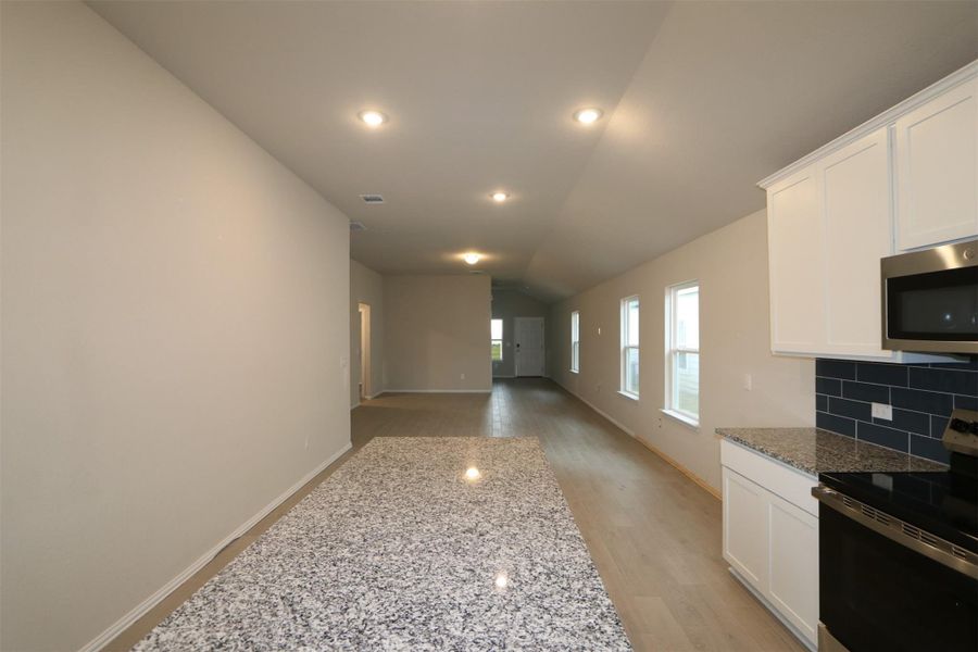 Kitchen featuring stainless steel appliances, decorative backsplash, lofted ceiling, white cabinets, and light stone counters