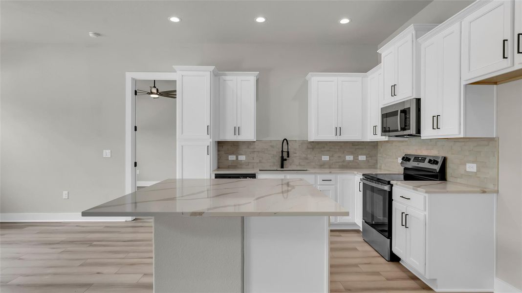 Kitchen with stainless steel appliances, light stone counters, white cabinets, a kitchen island, and recessed lighting