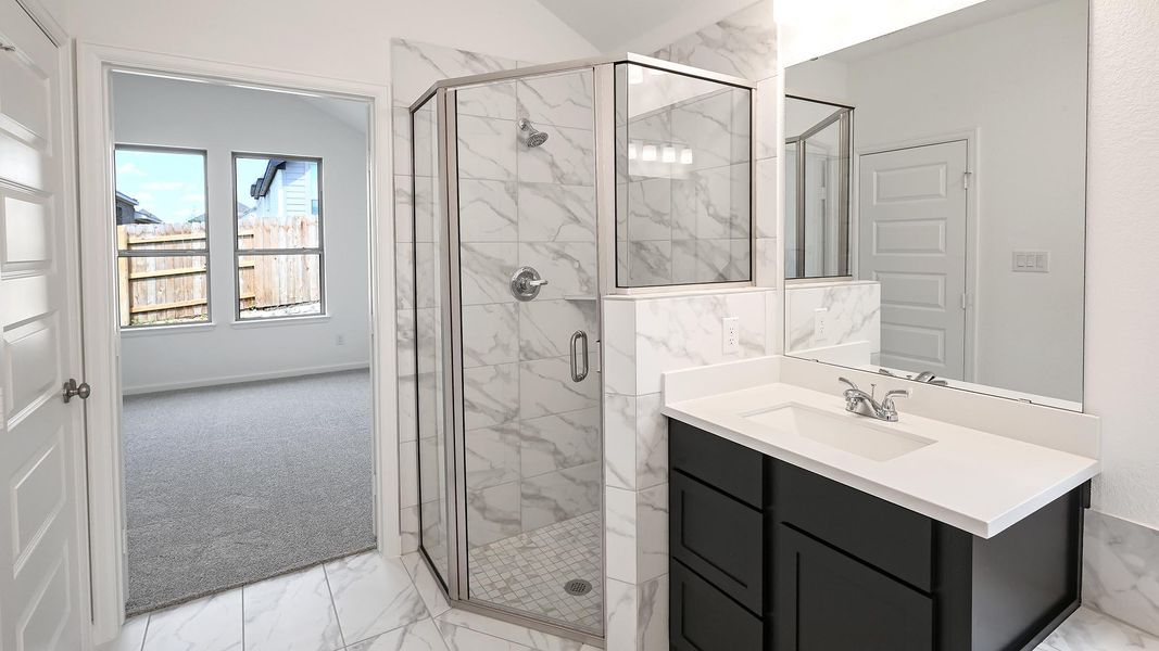Bathroom with light marble finish flooring, a stall shower, vanity, and vaulted ceiling Bathroom with light marble finish flooring, a stall shower, vanity, and vaulted ceiling