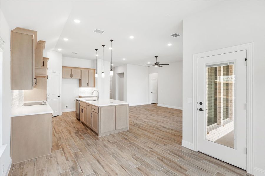 Open kitchen with center island, light wood cabinets, pendant lights, and wood-look tile floors opening to living area
