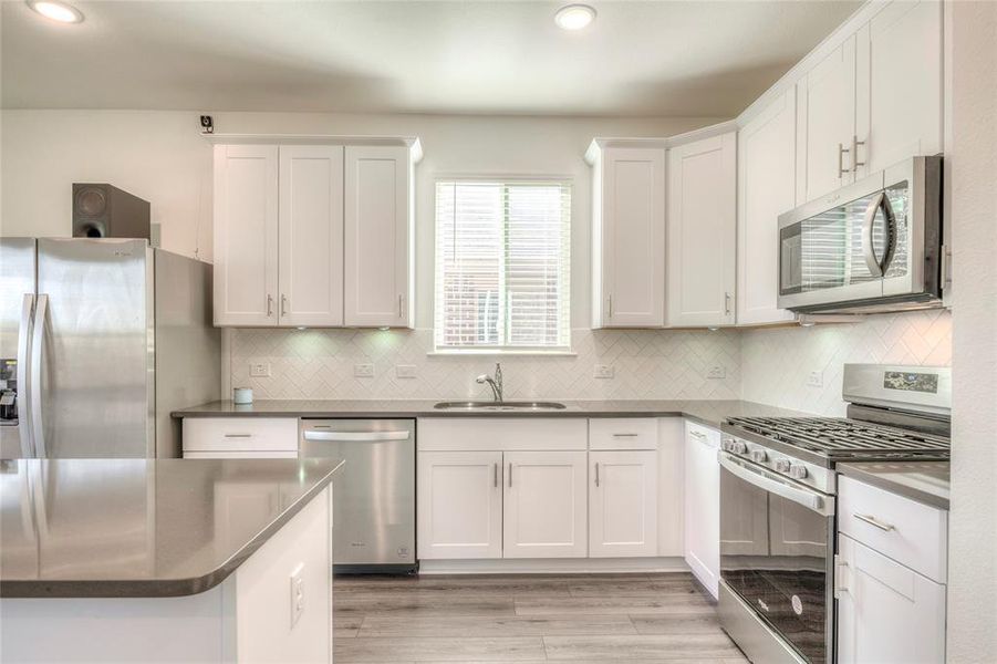 Kitchen with stainless steel appliances, white cabinetry, luxury vinyl plank flooring, subway tile backsplash, and recessed lighting Kitchen with stainless steel appliances, white cabinetry, luxury vinyl plank flooring, subway tile backsplash, and recessed lighting