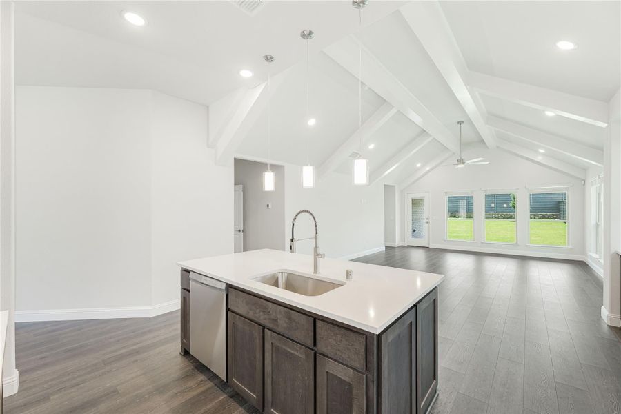 Kitchen island with sink and dark cabinets, open to living area with vaulted beam ceiling and hardwood floors Kitchen island with sink and dark cabinets, open to living area with vaulted beam ceiling and hardwood floors