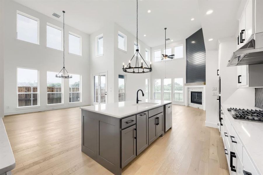 Open-concept living area featuring a kitchen island with stone countertop, wood-finish flooring, a contemporary fireplace with a shiplap accent wall, high ceilings, and abundant natural light from numerous windows