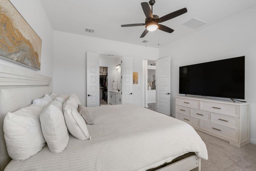 Main bedroom with visible vents, light carpet, ensuite bath, and a ceiling fan