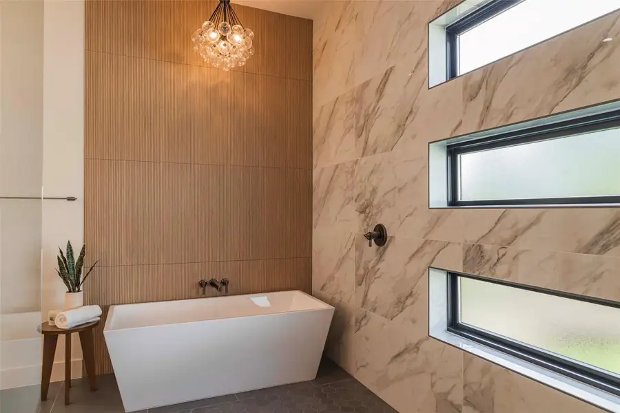 Full bathroom featuring a chandelier, a soaking tub, and tile walls