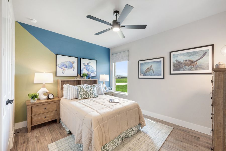 Bedroom with blue and green geometric accent wall, ceiling fan, hardwood floors, and wood furniture