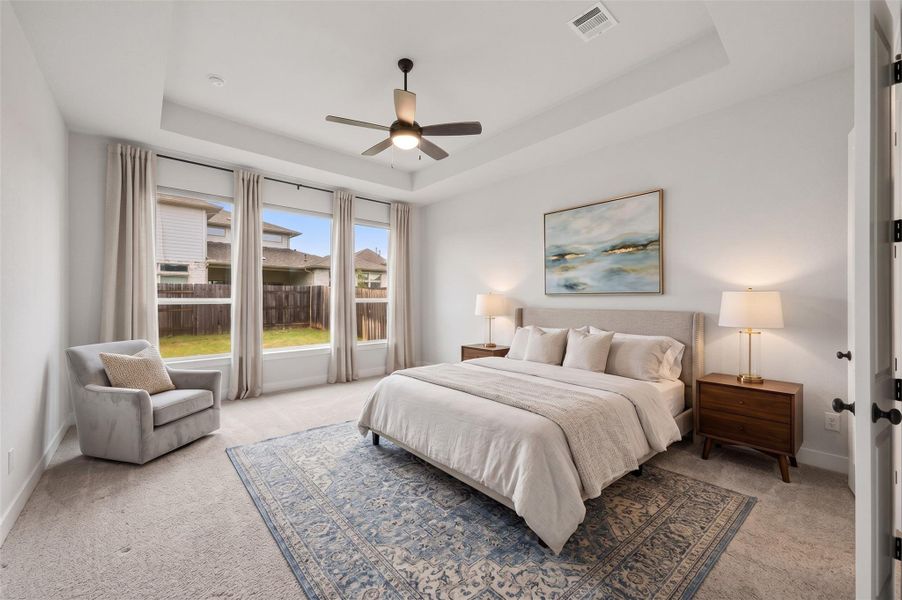 The primary bedroom creates a serene retreat with an elegant pop-up ceiling that adds architectural interest, complemented by plush carpeting for warmth and comfort. A ceiling fan with integrated lighting completes the space with a sophisticated, well-appointed feel and plenty of room for a sitting area. This photo has been virtually staged.