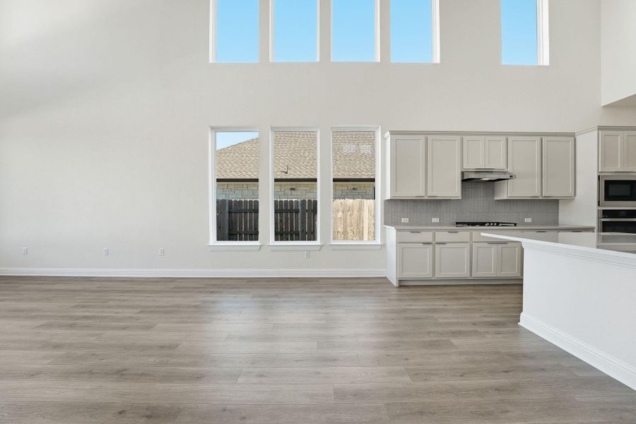 Kitchen featuring tasteful backsplash, light wood-style floors, white cabinetry, appliances with stainless steel finishes, and a towering ceiling