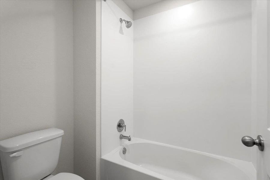Bathroom featuring a white bathtub, integrated shower, toilet, and chrome fixtures