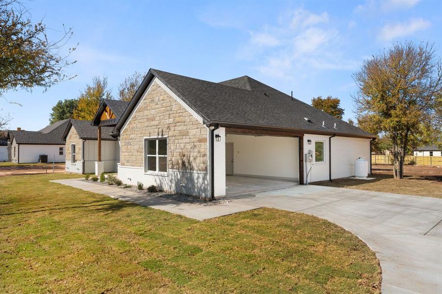 View of side of home with stone siding, roof with shingles, driveway, and an attached garage