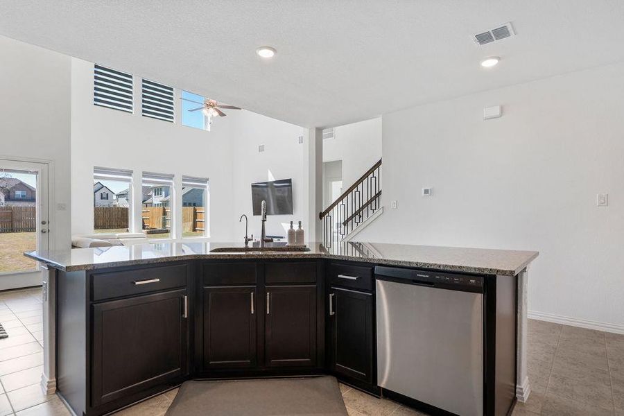 Kitchen featuring stainless steel dishwasher, a kitchen island with sink, a ceiling fan, open floor plan, and a high ceiling Kitchen featuring stainless steel dishwasher, a kitchen island with sink, a ceiling fan, open floor plan, and a high ceiling