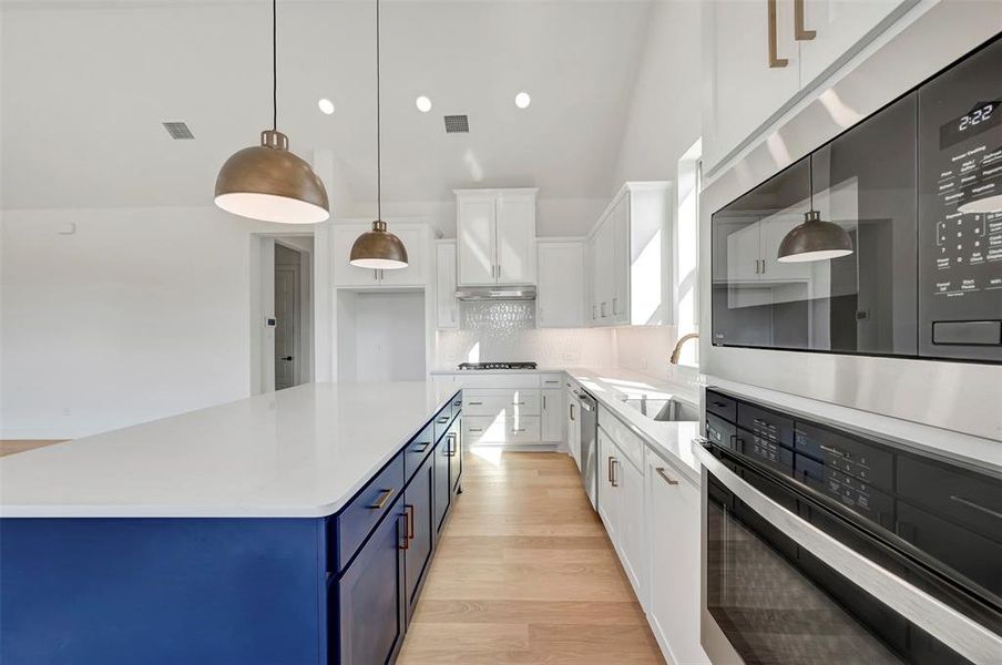 Kitchen featuring stainless steel appliances, dual tone cabinets, tasteful backsplash, light stone countertops, and hanging light fixtures Kitchen featuring stainless steel appliances, dual tone cabinets, tasteful backsplash, light stone countertops, and hanging light fixtures