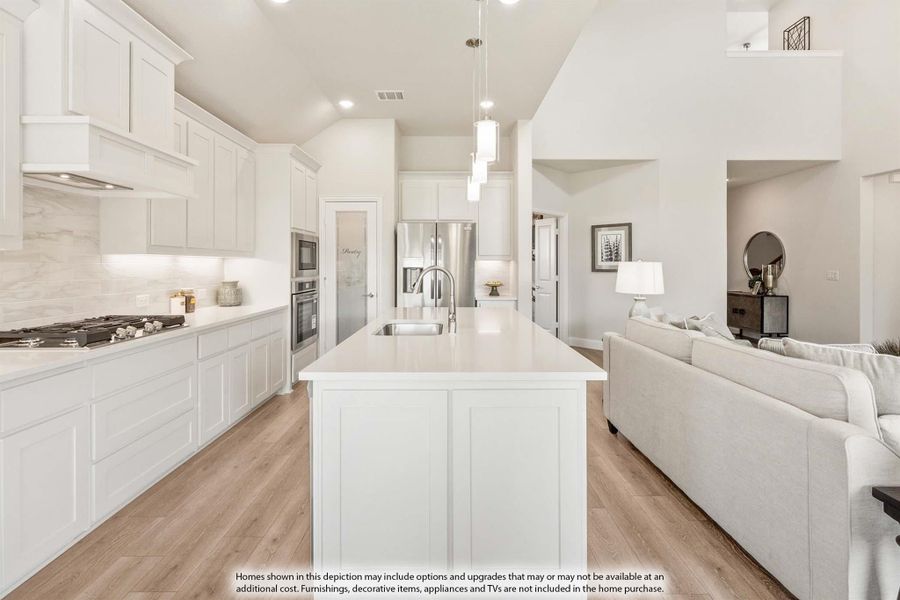 Open kitchen with white cabinets, large island, stainless appliances, and pendant lights, open to living room with hardwood floors