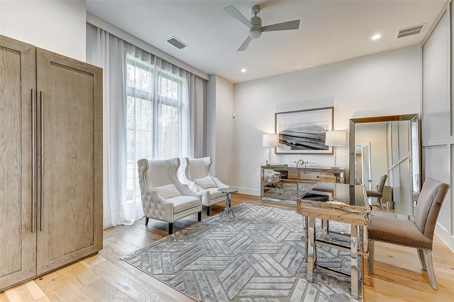 This bright and stylish room features elegant seating, a modern glass-top desk, and a large window with sheer curtains, offering plenty of natural light. The neutral color palette and contemporary decor create a welcoming and sophisticated atmosphere, ideal for a home office or relaxing space.