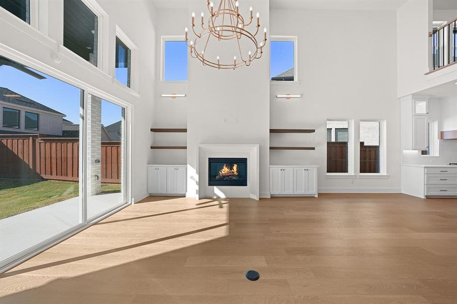 Unfurnished living room featuring a glass covered fireplace, light wood-style flooring, a towering ceiling, and a chandelier Unfurnished living room featuring a glass covered fireplace, light wood-style flooring, a towering ceiling, and a chandelier