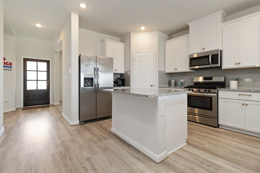 Open kitchen with white cabinets, granite countertops, stainless steel appliances, and light wood flooring Open kitchen with white cabinets, granite countertops, stainless steel appliances, and light wood flooring