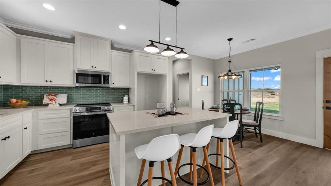 Kitchen with appliances with stainless steel finishes, a breakfast bar area, a kitchen island, white cabinets, and dark wood finished floors