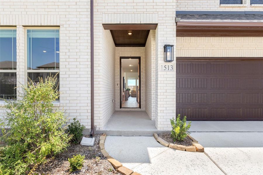 Front entry of home 1513 with open door, wood-covered porch, white brick exterior, and attached garage