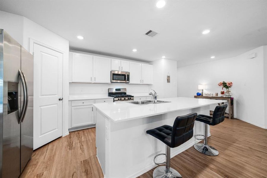 A modern kitchen with white cabinets, stainless steel appliances, quartz countertops, and a large island with bar seating.