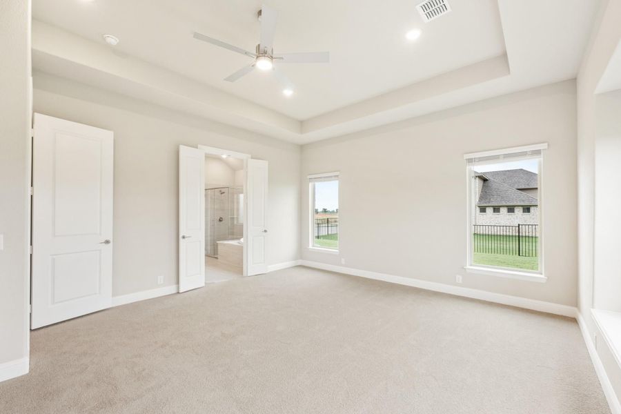 Spacious master bedroom with tray ceiling, ceiling fan, carpet flooring, and ensuite bathroom access