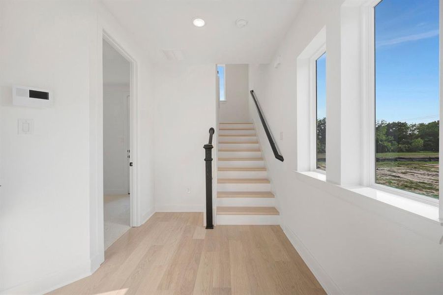 Entryway featuring wood-finish flooring, a contemporary staircase with black wrought iron baluster, bright white walls, and multiple windows