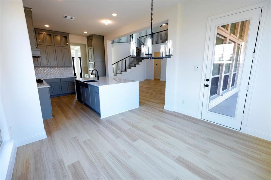 Kitchen with decorative backsplash, a kitchen island with sink, glass insert cabinets, light wood-style floors, and light stone counters Kitchen with decorative backsplash, a kitchen island with sink, glass insert cabinets, light wood-style floors, and light stone counters