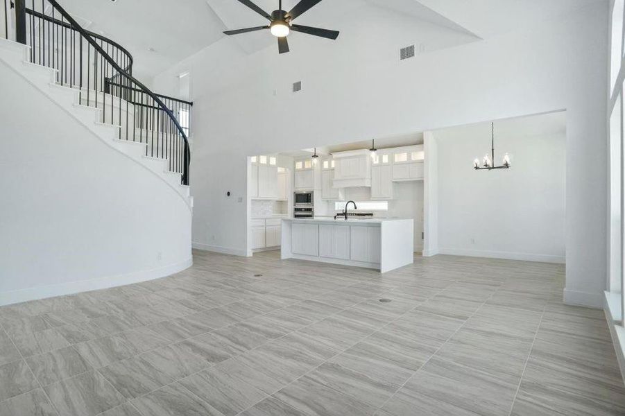 Unfurnished living room featuring high vaulted ceiling, sink, and ceiling fan with notable chandelier