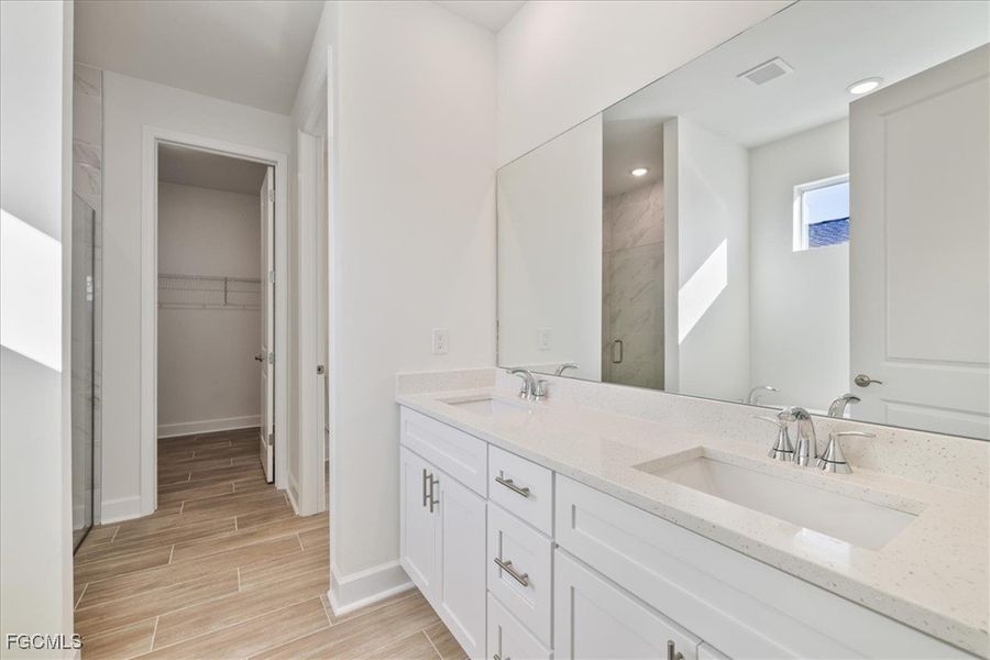 Full bathroom with a stall shower, double vanity, a walk in closet, and wood finish floors