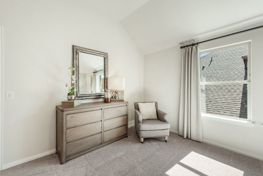 Bedroom with wood dresser, framed mirror, gray accent chair, and large window with curtains