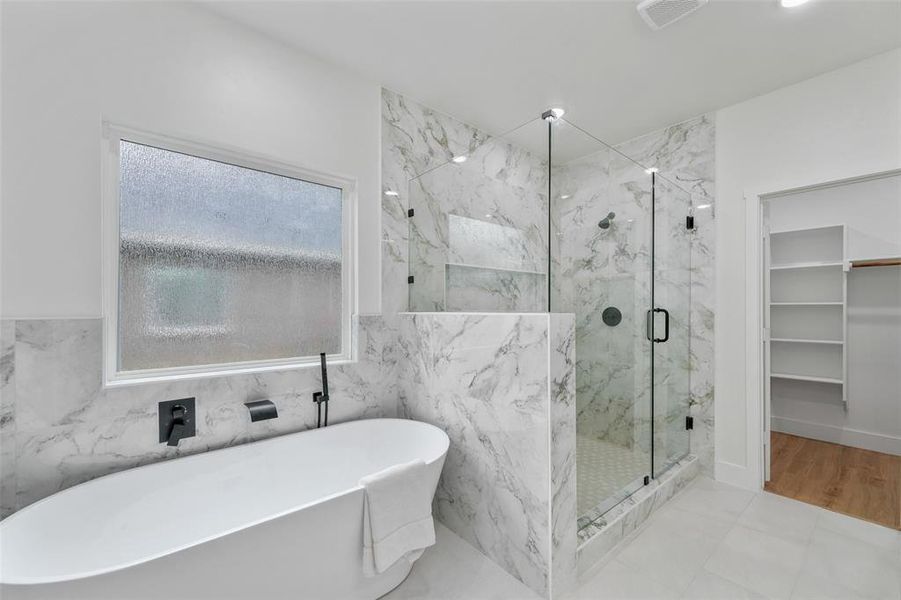 Bathroom featuring a freestanding soaking tub with matte black fixtures, a spacious glass-enclosed shower with marble-patterned tile, and light-colored flooring Bathroom featuring a freestanding soaking tub with matte black fixtures, a spacious glass-enclosed shower with marble-patterned tile, and light-colored flooring