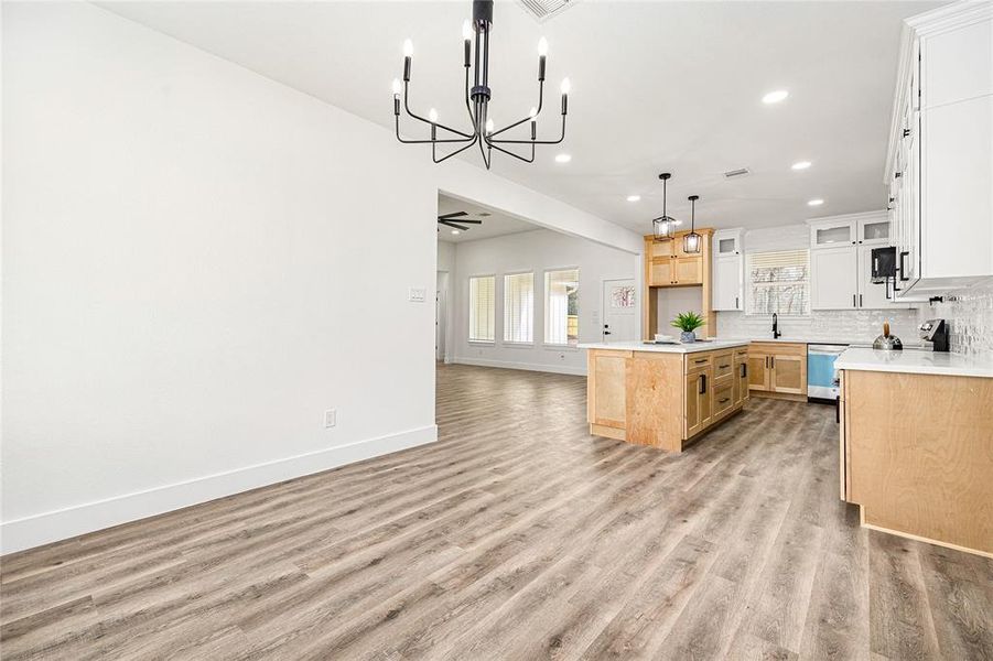 This photo showcases a bright, open-concept kitchen and dining area with wood flooring, modern light fixtures, and a spacious island. The kitchen features white cabinetry, large windows, and stainless steel appliances, creating a welcoming and functional space.