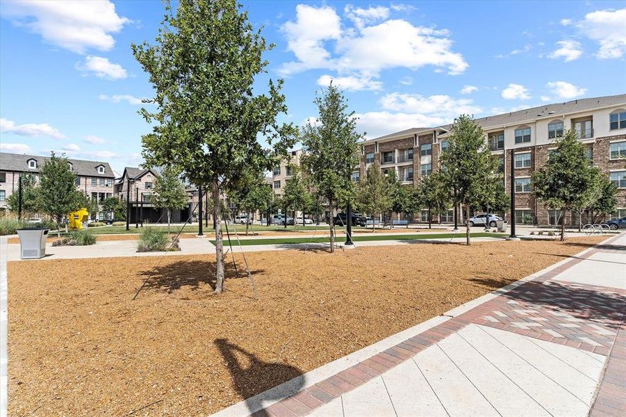 Expansive common area featuring a central wood chip ground cover, mature trees, and patterned hardscaping Expansive common area featuring a central wood chip ground cover, mature trees, and patterned hardscaping