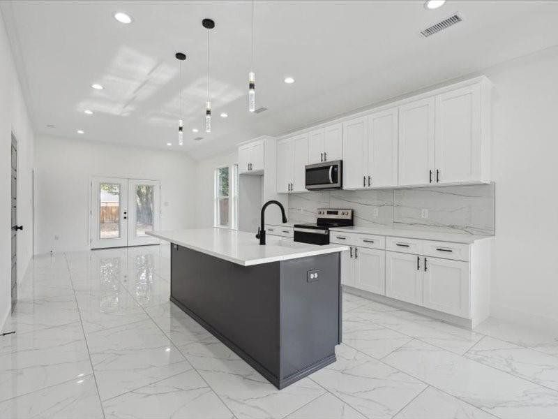 Kitchen with stainless steel appliances, a center island with sink, tasteful backsplash, and white cabinetry