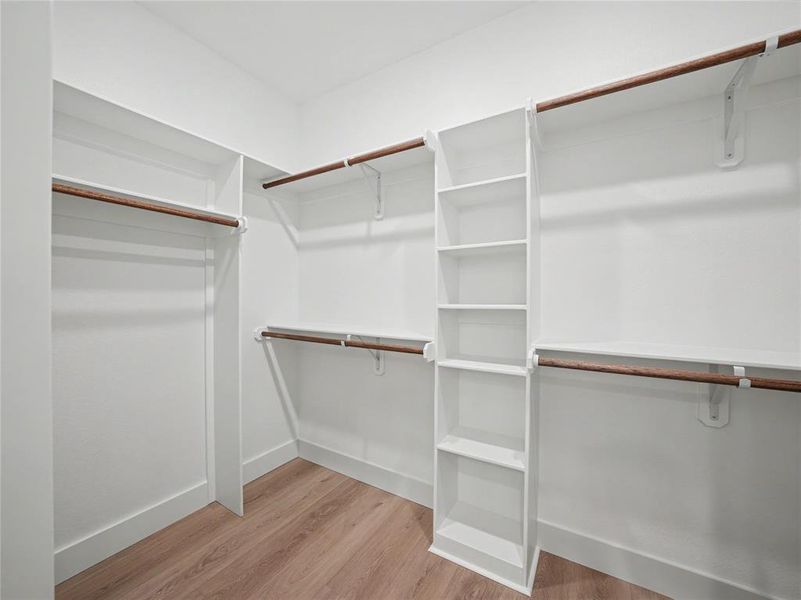 Walk-in closet featuring built-in shelving, multiple hanging rods, white walls, and wood-finish flooring Walk-in closet featuring built-in shelving, multiple hanging rods, white walls, and wood-finish flooring