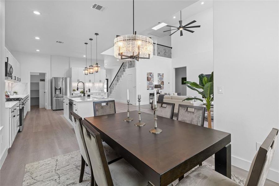 Dining area featuring a chandelier, stairs, light wood finished floors, ceiling fan, and a towering ceiling Dining area featuring a chandelier, stairs, light wood finished floors, ceiling fan, and a towering ceiling
