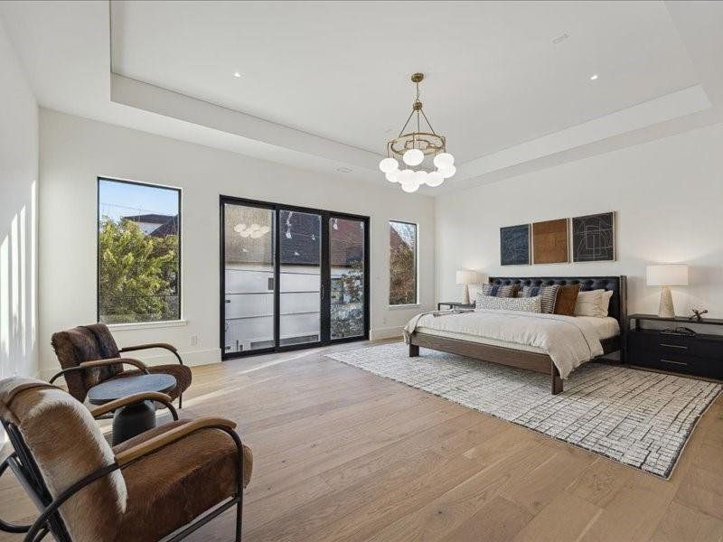 The spacious primary bedroom features large windows that fill the room with natural light and open to a beautiful private balcony, complemented by a modern chandelier.