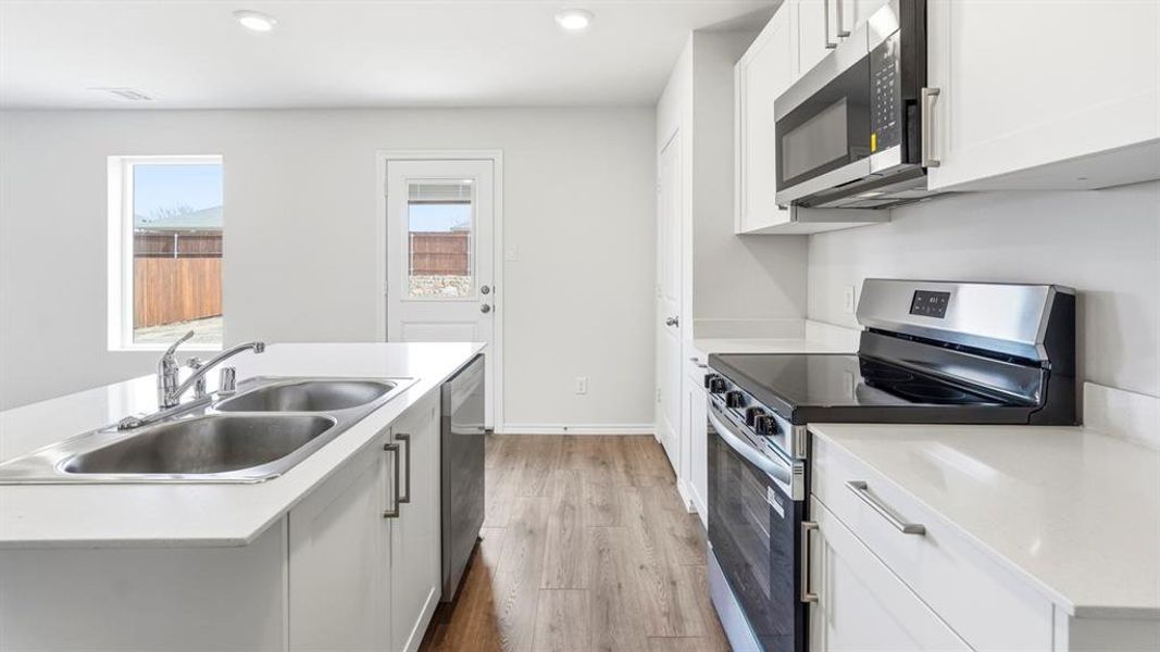 Kitchen with stainless steel appliances, light countertops, white cabinetry, a kitchen island with sink, and recessed lighting
