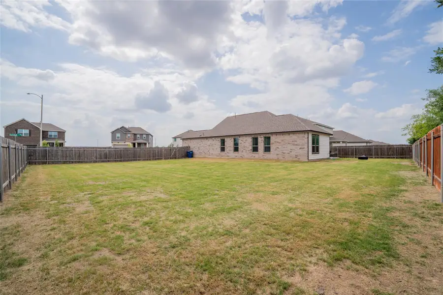 Expansive fenced backyard featuring a single-story brick exterior, multiple windows, and a shingled roof Expansive fenced backyard featuring a single-story brick exterior, multiple windows, and a shingled roof