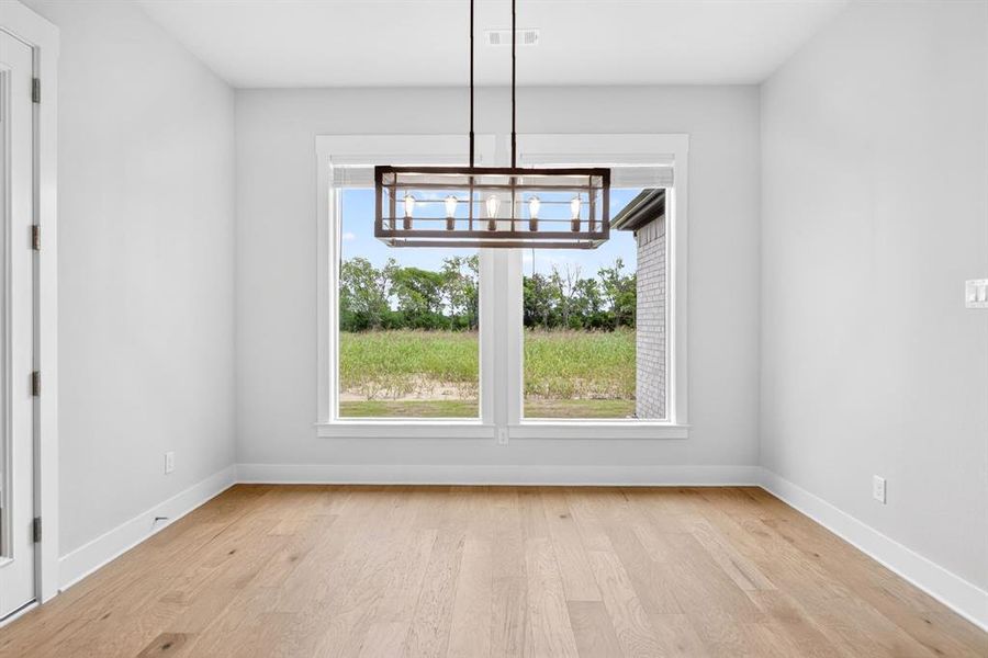 Spacious room featuring wood-finish flooring, white baseboards, and a modern rectangular chandelier Spacious room featuring wood-finish flooring, white baseboards, and a modern rectangular chandelier