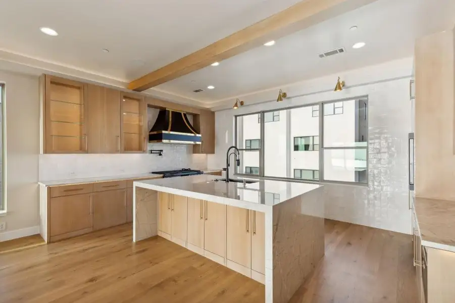Kitchen with premium range hood, a sink, light wood-type flooring, decorative backsplash, and a large island