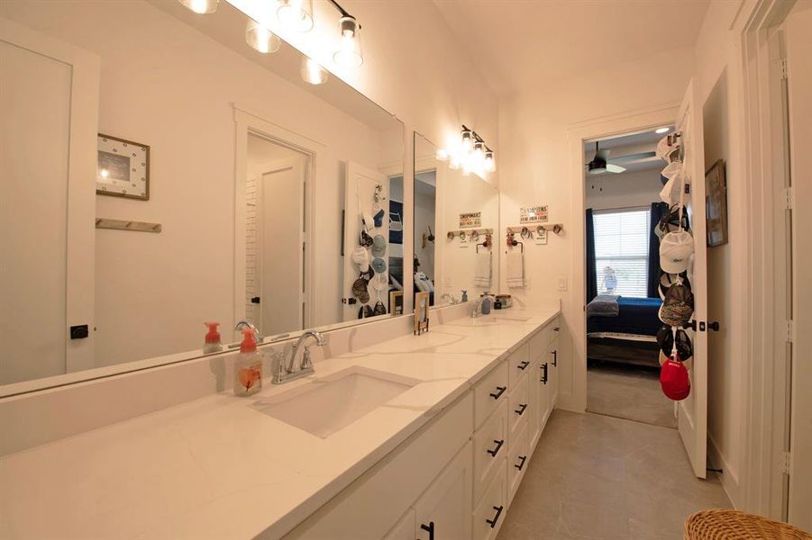 Ensuite bathroom featuring double vanity, light tile patterned floors, and a ceiling fan