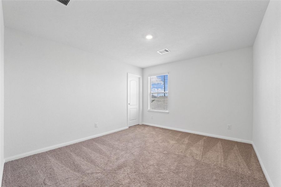 This secondary bedroom offers comfort and style with plush carpeting, neutral paint tones, recessed lighting, a large window with blinds, and a generously sized closet.
