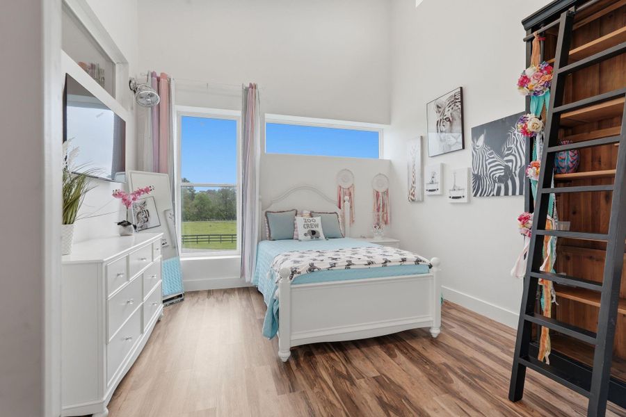 Bright and airy bedroom with large windows offering scenic views. Features a cozy bed, stylish decor with zebra artwork, and a ladder leading to a loft area. Warm wood flooring complements the white furniture, creating an inviting atmosphere.