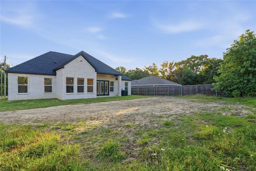 Rear elevation featuring light brick siding, multiple windows, a dark shingle roof, and double patio doors