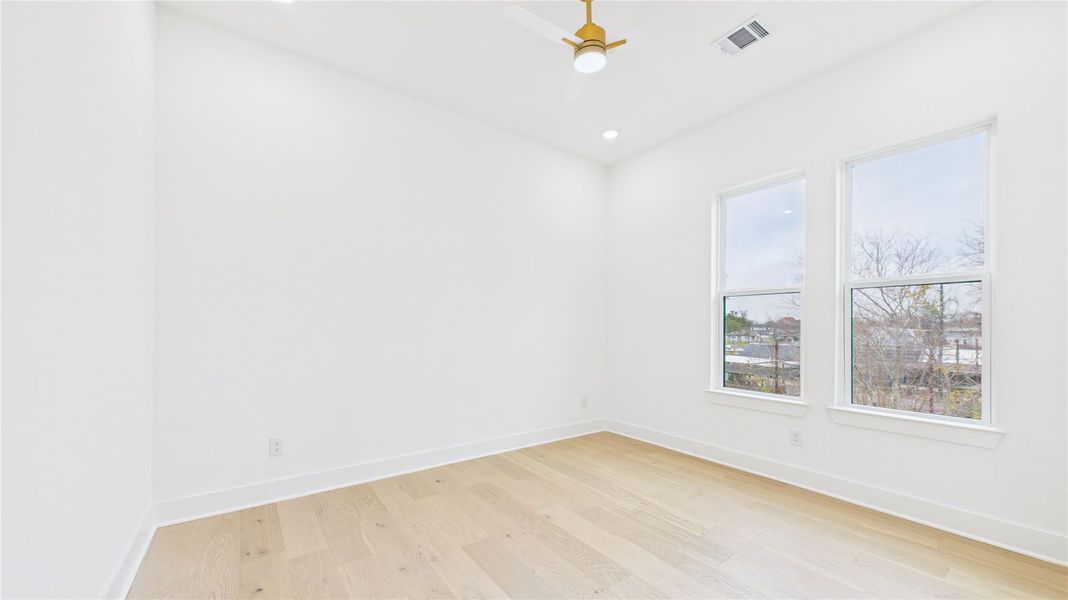 This photo shows a secondary bedroom featuring two large windows allowing natural light, a ceiling fan, and recessed lighting, creating an airy and spacious feel.