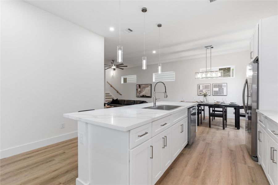 Clean, modern living with an open-concept layout, oversized quartz island, and seamless flow into the dining and living areas. High ceilings, warm tone flooring, and sleek finishes create a bright, inviting space built for both everyday living and entertaining.