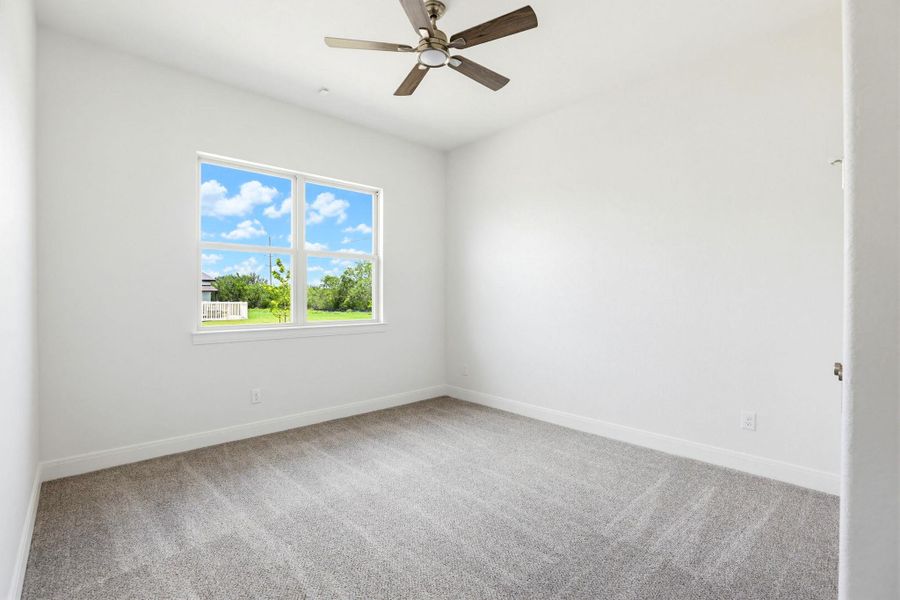 A well-lit bedroom features plush carpeting and a modern ceiling fan, offering tranquil views.