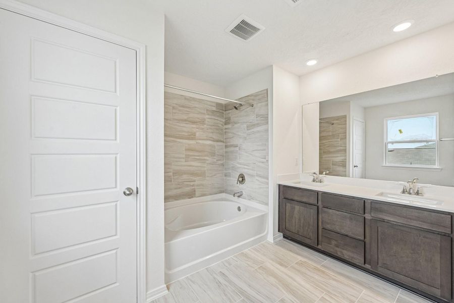 This stunning primary bathroom is truly move-in ready! It features stained cabinetry with light countertops, dual sinks, a large mirror, high ceilings, custom paint, a large window, and sleek modern finishes throughout.