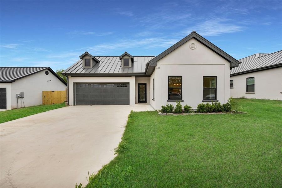 Modern inspired farmhouse with concrete driveway, a front lawn, an attached garage, a standing seam roof, and metal roof Modern inspired farmhouse with concrete driveway, a front lawn, an attached garage, a standing seam roof, and metal roof
